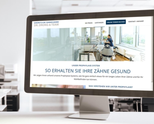 Desktopmonitor auf Schreibtisch zeigt Website von Zahnarztpraxis Drong. Hintergrund Büro.